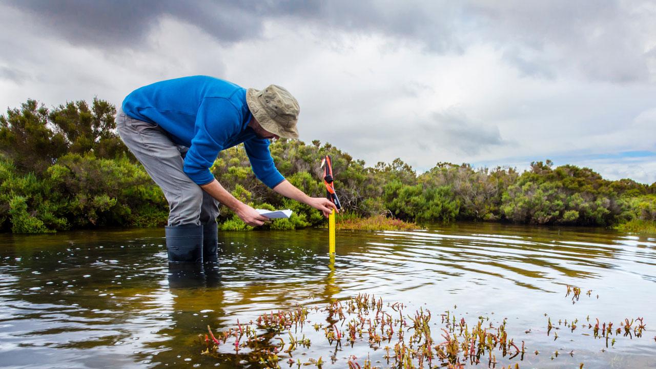 An employee standing in mid-calf high water takes measurements